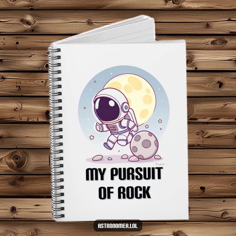 Funny notebook with a cartoon astronaut playfully chasing a rolling moon rock on the cover, ideal for note-taking.